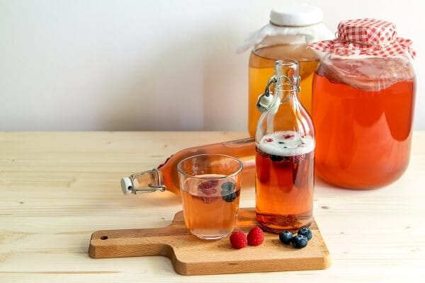 Garrafas de diferentes bebidas fermentadas, como kombucha, kefir e vinagre de maçã, dispostas sobre uma mesa.